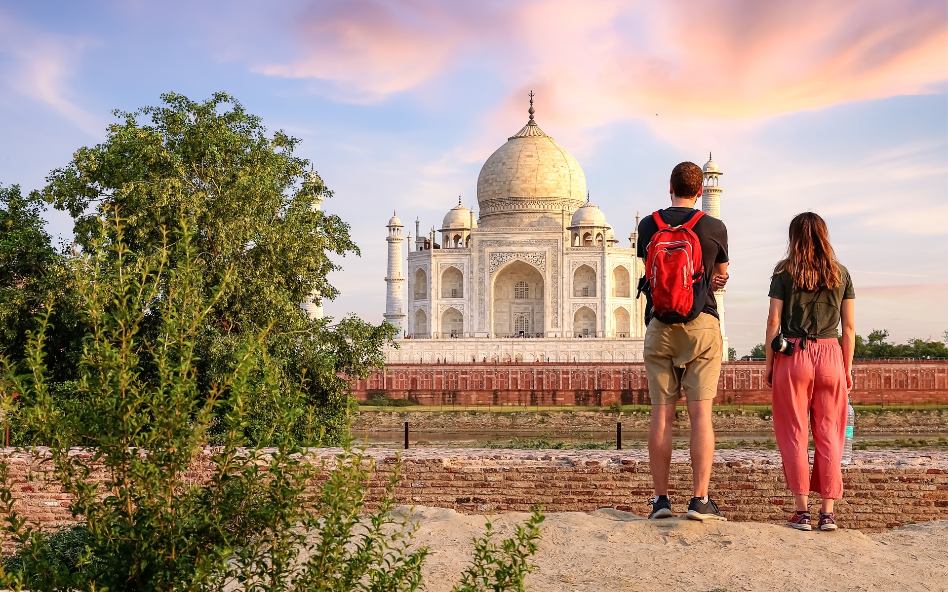 Tourist couple enjoy view of the historic Taj Mahal at sunset from Mehtab Bagh at Agra India