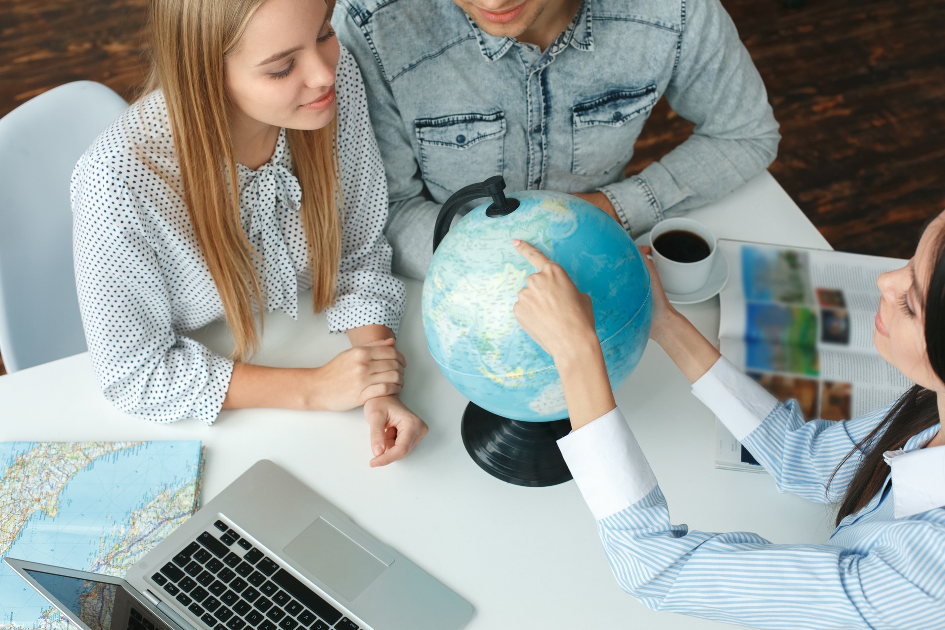 Young couple in a tour agency communication with a travel agent travelling concept destination on a globe